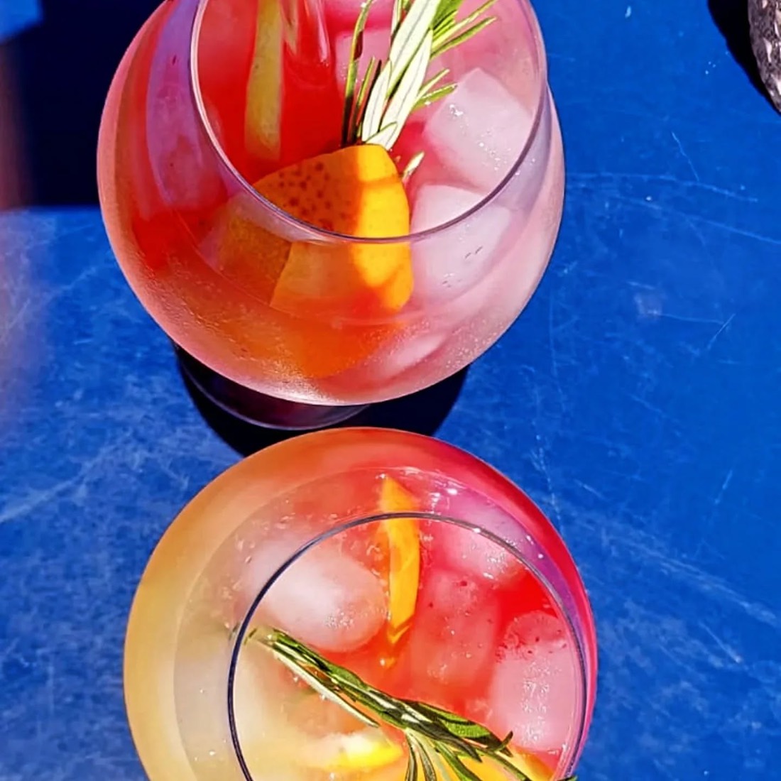 Zwei rosafarbene Apéro-Drinks mit Rosmarin, Orange und Eis, von oben fotografiert