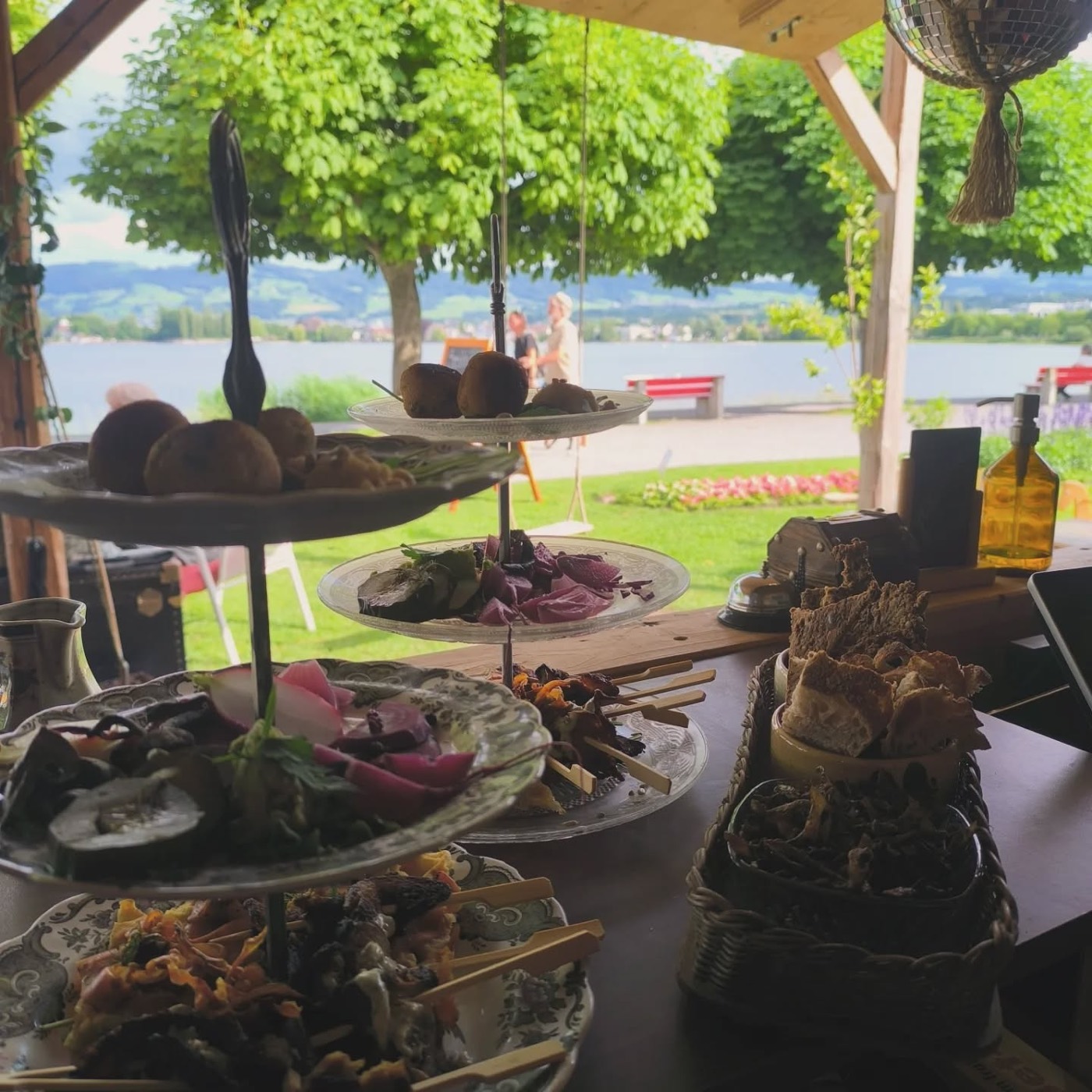 Dreistöckige Etagere mit pflanzlichen Köstlichkeiten, im Hintergrund der Bodensee mit Wiese und Schaukel
